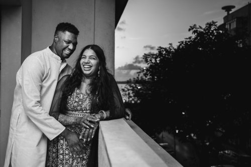 Bride and groom laughing together during candid black and white couple portrait in their mumbai apartment during mehendi overlooking the mumbai sea