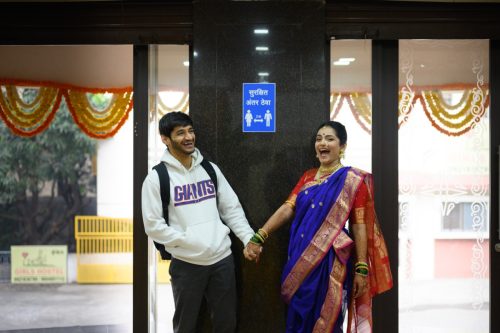 Bride and groom holding hands while laughing during candid wedding couple portraits looking at a board showing corona virus warning of distancing in pune