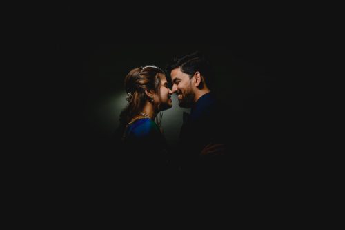 Bride and groom standing close together during dramatic low light wedding couple portrait lit by a backlight smiling affectionately, vishnukrupa hall, pune