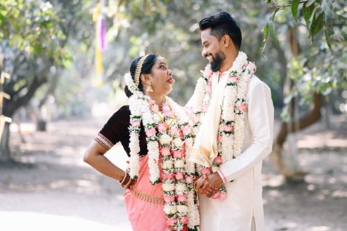 Bride making funny expression and teasing the groom while wearing tamil wedding wearing garlands during couple portraits at Ecoville, Pune