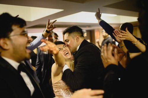 Groom kissing bride while she laughs during cocktail party with friends cheering in Pune wedding