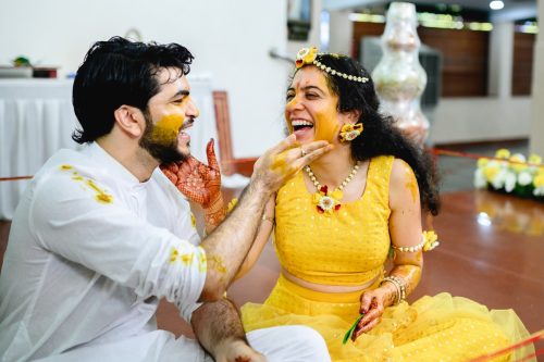 bride and groom laughing as the groom puts haldi on bride's face