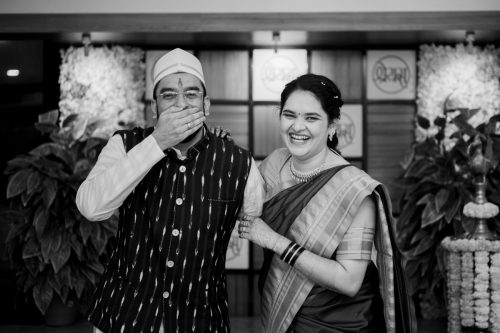 Bride laughing while groom covers his mouth during black and white couple portrait. Maharashtrian wedding at Shreyas hall