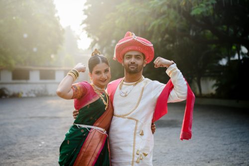 Bride and groom posing playfully as body builders in traditional Maharashtrian wedding attire