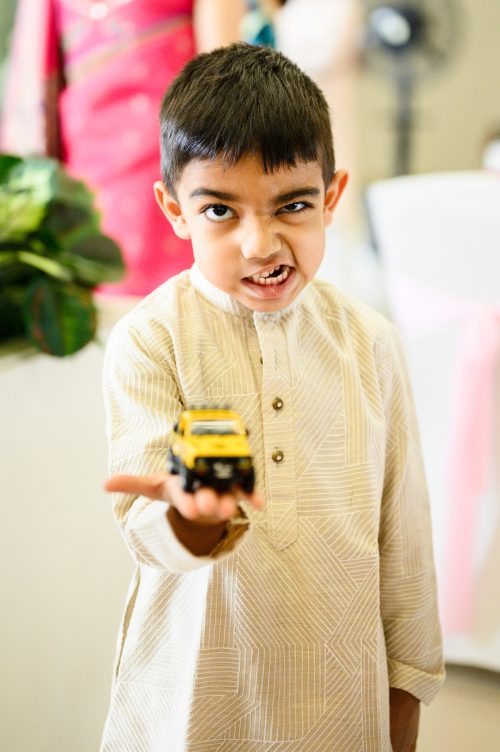 Young nephew making a funny face while holding toy car at wedding in Pune