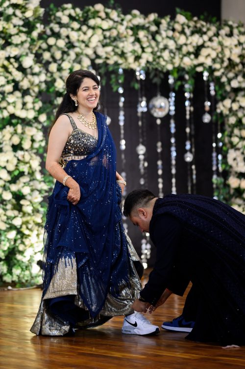 Groom adjusting bride’s shoes during sangeet while she laughs on stage in Pune wedding