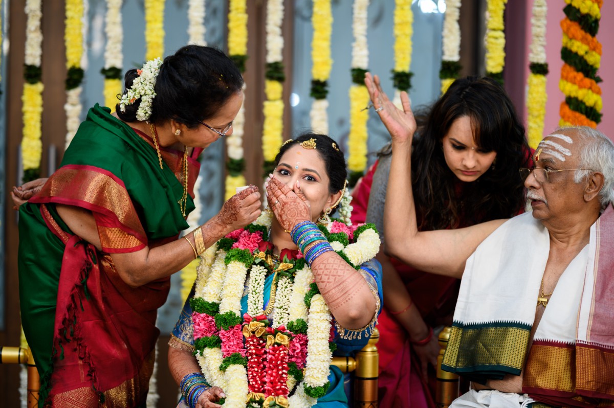 Bride smiling reacting playfully as family performs wedding rituals on the mandap during a tam bram wedding rituals